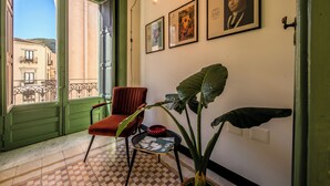 A room with a red chair, a table with a magazine, a large plant, and framed pictures on the wall. - Palazzo Villelmi (Cefalù)