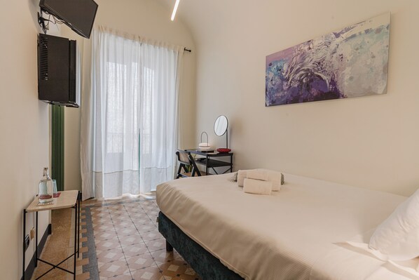 A bedroom with a bed, a desk with a chair, a TV, and a painting on the wall.