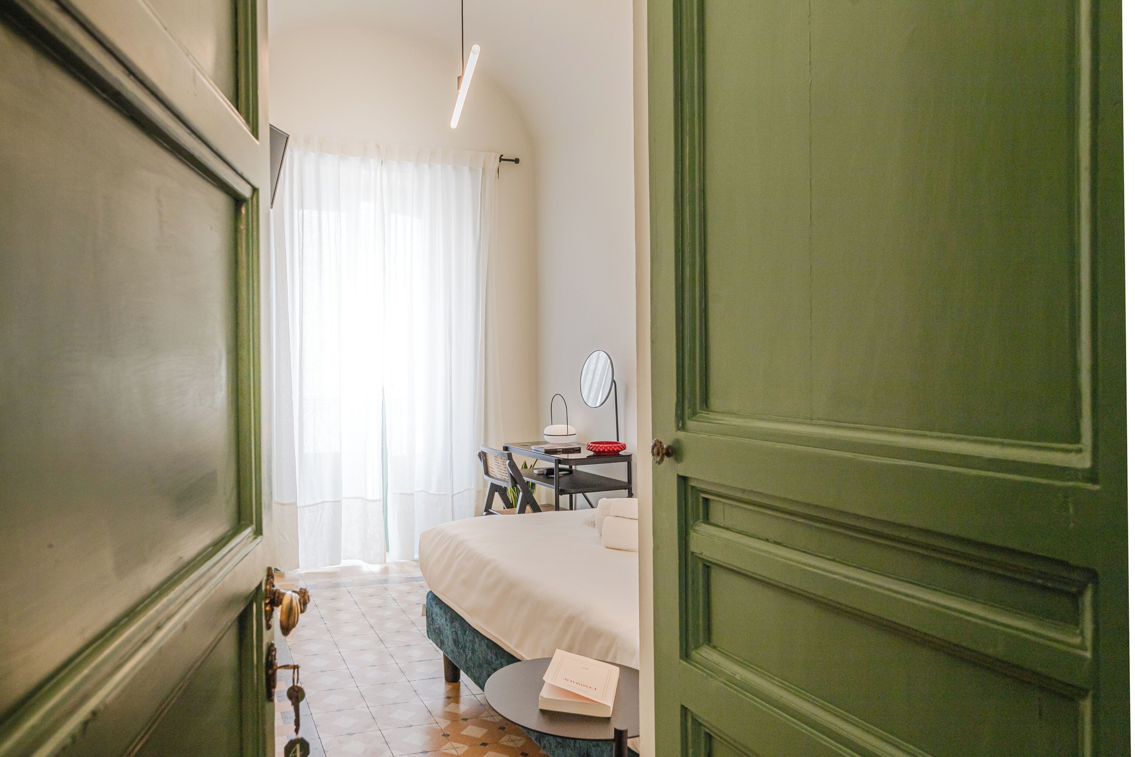 A bedroom with a bed, a desk, a chair, a round table, a mirror, and a door.