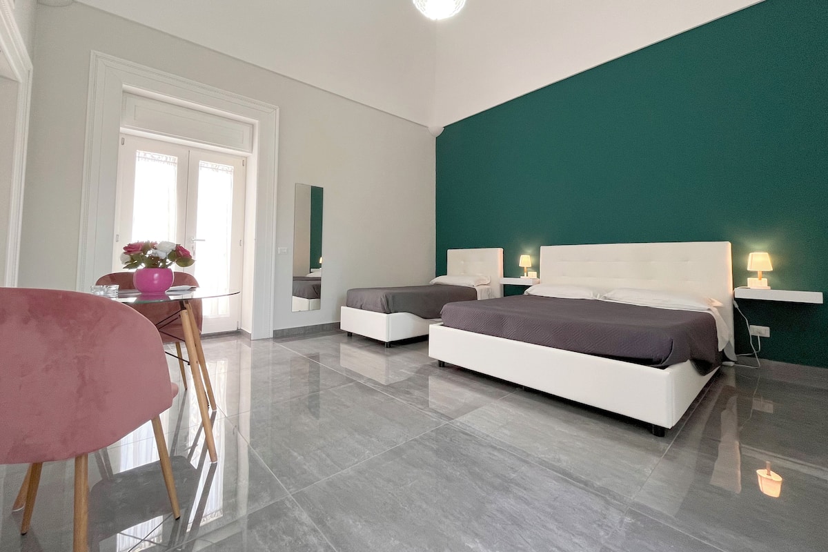 A modern hotel room with a large bed, two bedside tables, a desk with a chair, and a mirror.