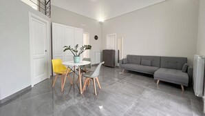 A spacious living area with a grey sofa, a round table with chairs, and a potted plant. - DC House (Procida)
