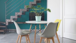 A modern interior with a staircase against a teal wall, a round table with chairs, and a potted plant. - DC House (Procida)