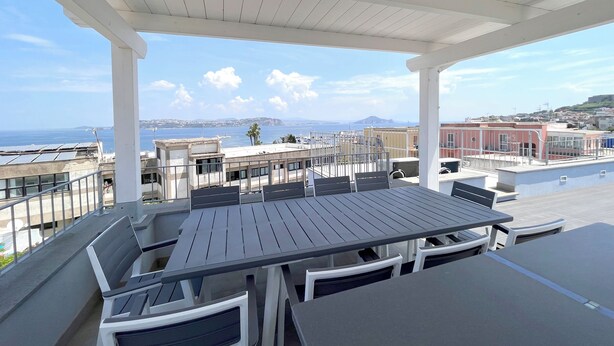 An outdoor terrace with a table and chairs, overlooking a coastal cityscape. - DC House (Procida)