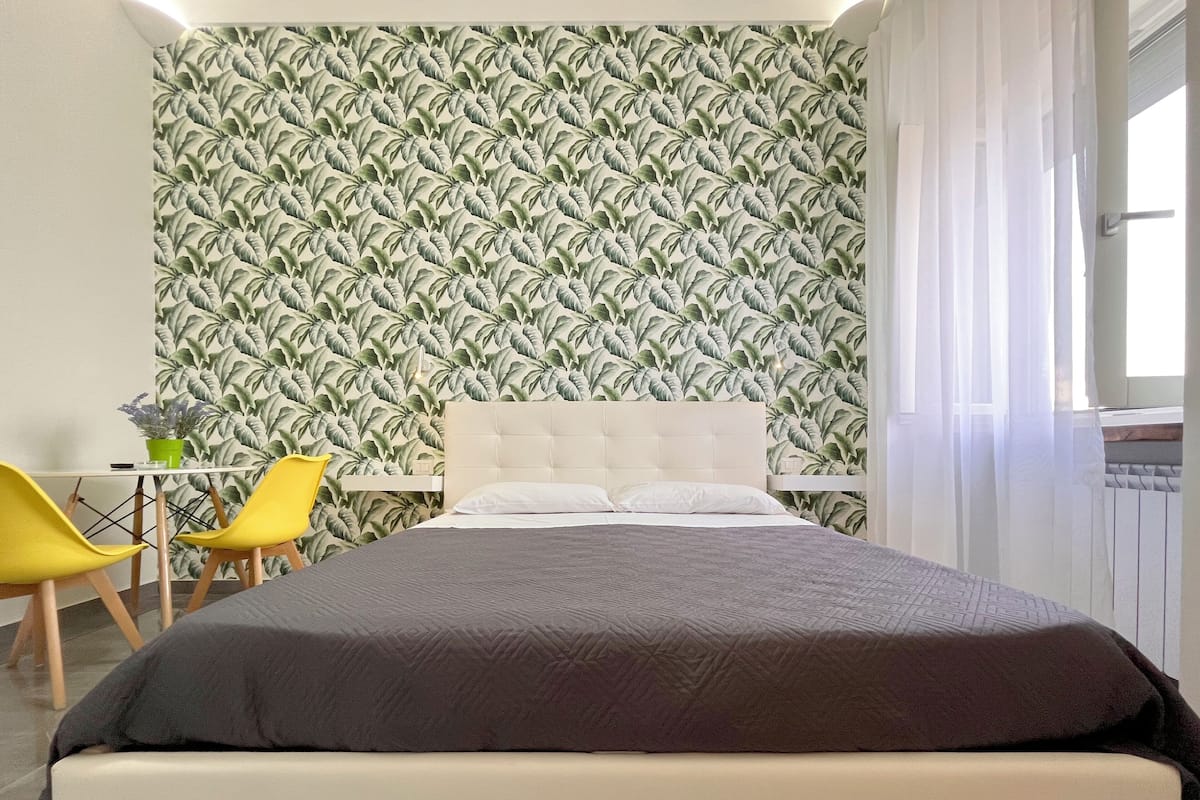 A bedroom with a bed, a nightstand, a chair, and a wall with a leaf pattern.
