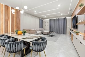 A modern living room with a dining area, a sofa set, and a TV mounted on the wall.