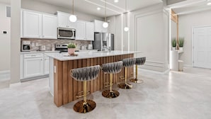 A modern kitchen with white cabinets, stainless steel appliances, and a wooden island with bar stools. - 7BR house sleeps 24 with game room (Clermont)