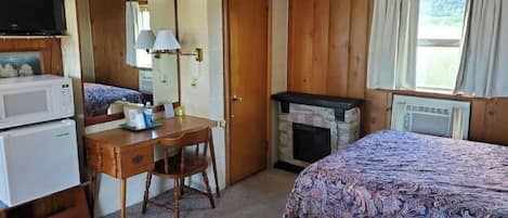 Una habitación con cama, escritorio, televisor, chimenea y ventana con cortinas.