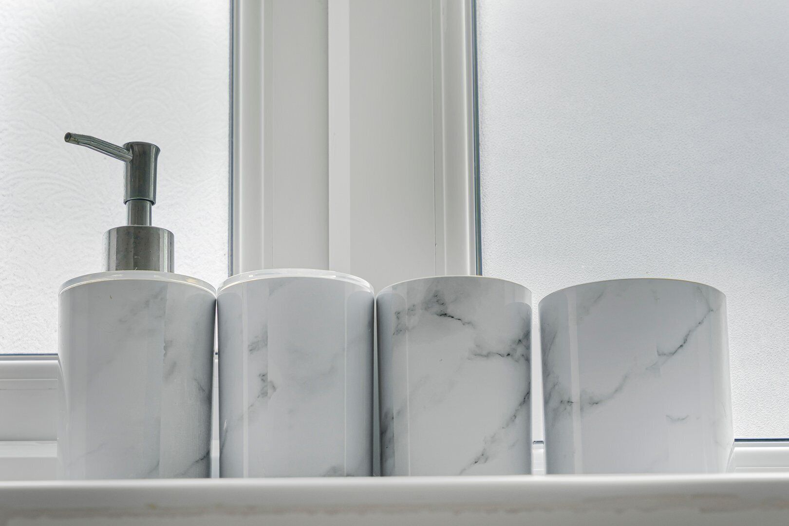 Une étagère de salle de bain avec trois distributeurs pour produits de salle de bain en marbre et un flacon à pompe.