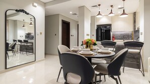 A modern dining area with a large mirror, a round table set for four, and a kitchen in the background.
