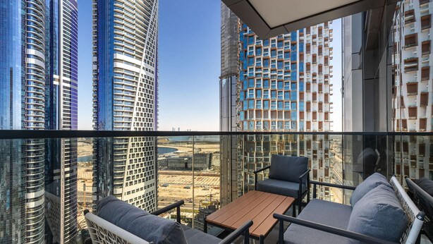 A balcony with a view of tall buildings, a wooden table, and two chairs.