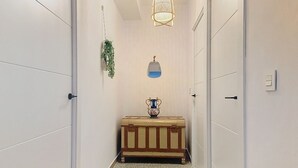 A narrow hallway with white walls, a wooden chest, a hanging plant, and a wall-mounted light fixture.