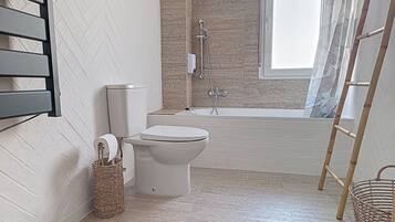 Un baño con inodoro, bañera, ducha y ventana.