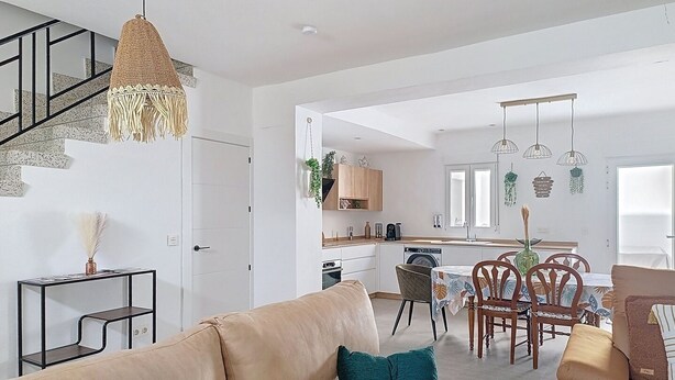 A modern living room with a sofa, a dining table with chairs, a kitchen area, and a staircase.