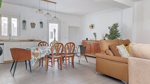 Cuina moderna amb armaris de fusta, taula de dinar amb caires i sofà a la zona saló.