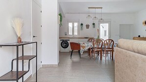 A modern kitchen with a washing machine, dining table with chairs, and a sofa in a living area.