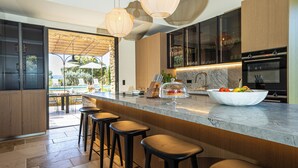 A modern kitchen with a marble countertop, bar stools, and a view of an outdoor pool area. - Luxury Mas in Gordes with pool & view Charming comfort and privacy (Gordes)
