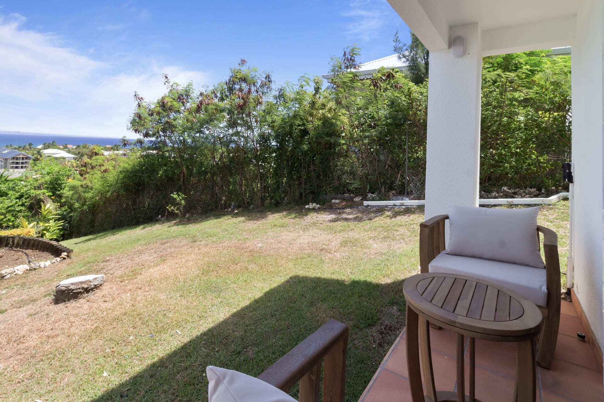 A covered outdoor seating area with a view of a grassy yard and trees.