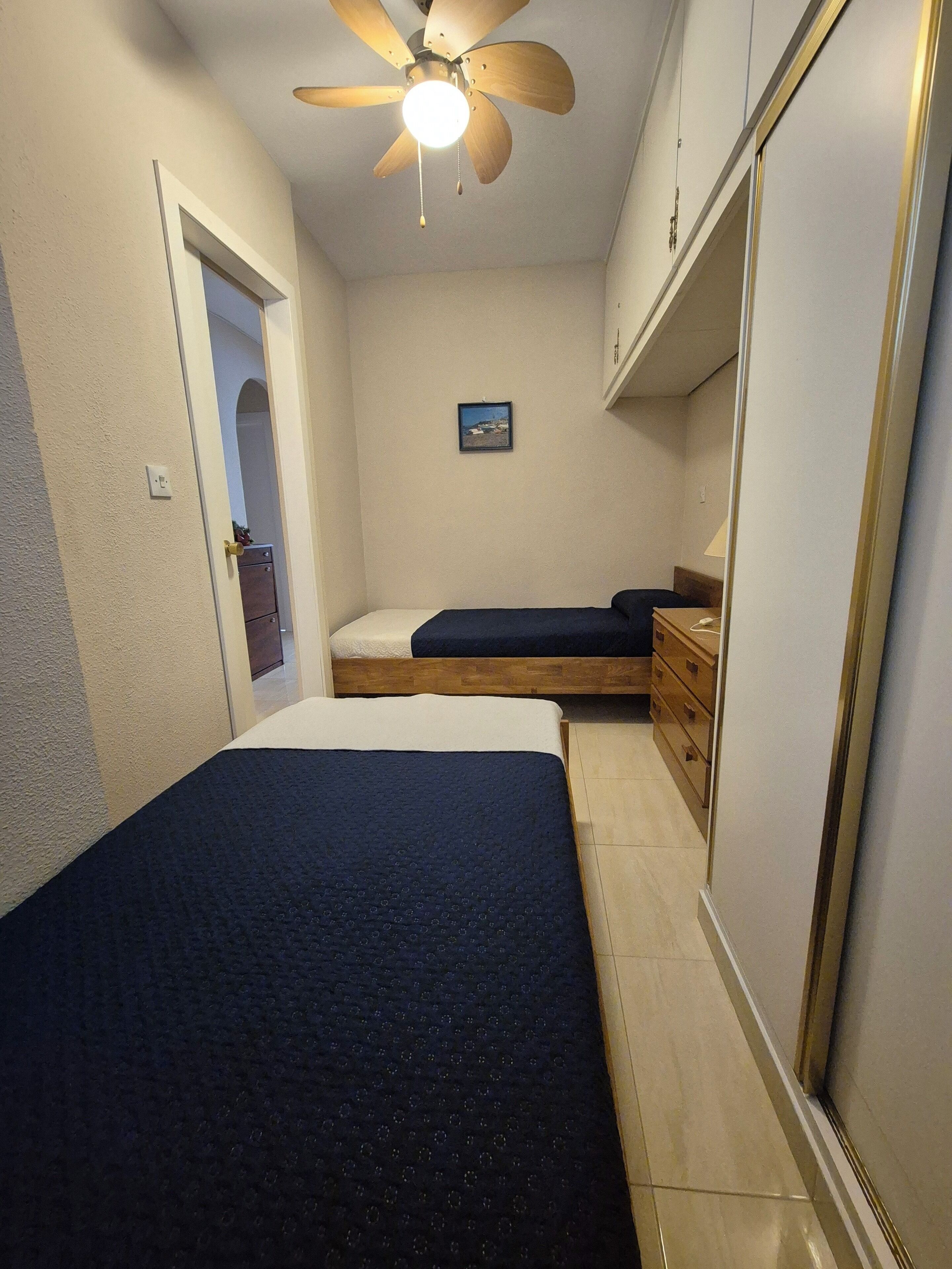 A bedroom with a bed, a nightstand, a dresser, a ceiling fan, and a small picture on the wall.