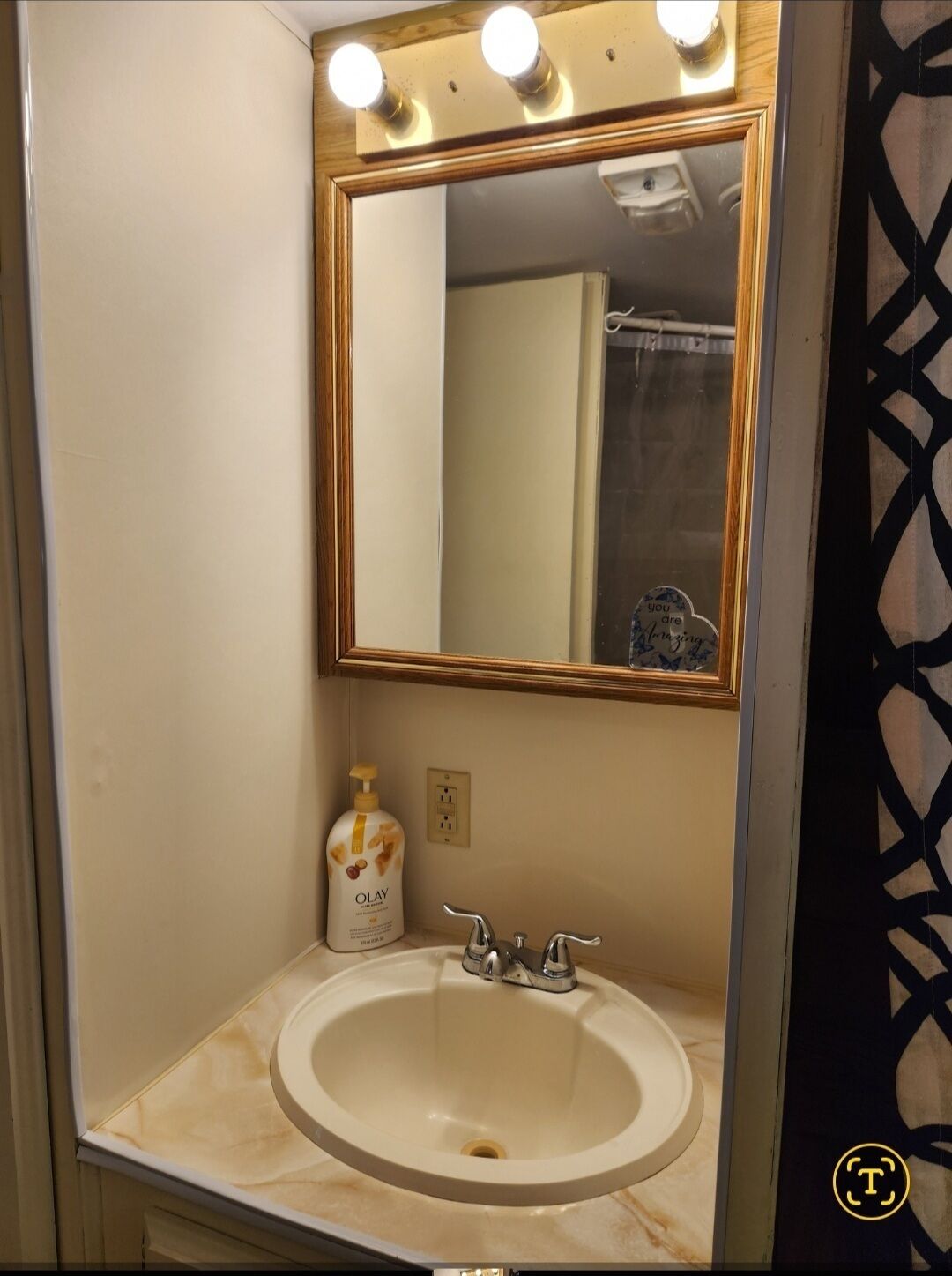 A bathroom with a white sink, a mirror with a gold frame, and a bottle of Olay soap.