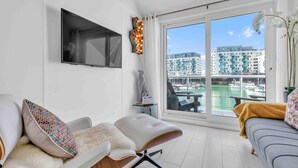 A modern living room with a sofa, a chair, a TV mounted on the wall, and a view of a marina through large windows. - On the Water 7| Free Parking | By My Getaways (Brighton)