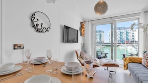 A dining area with a table set for four, a sofa, and a view of a marina through large windows. - On the Water 7| Free Parking | By My Getaways (Brighton)