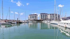 A marina with multiple boats docked, a clear sky, and buildings in the background. - On the Water 7| Free Parking | By My Getaways (Brighton)