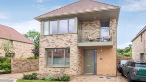A two-story brick house with a balcony, a garage with a car, and a well-maintained lawn.