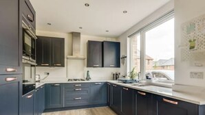A modern kitchen with dark cabinetry, a large window, and a wooden floor.