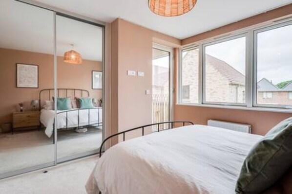 A bedroom with a bed, a window, and a door leading to another room.