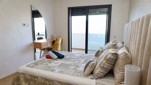 A bedroom with a bed, a desk, a chair, and a view of the sea. - 5mn from the beach, elegant relaxation apartment, Swimming pool, Playground, Park (Âïn-Harrouda)