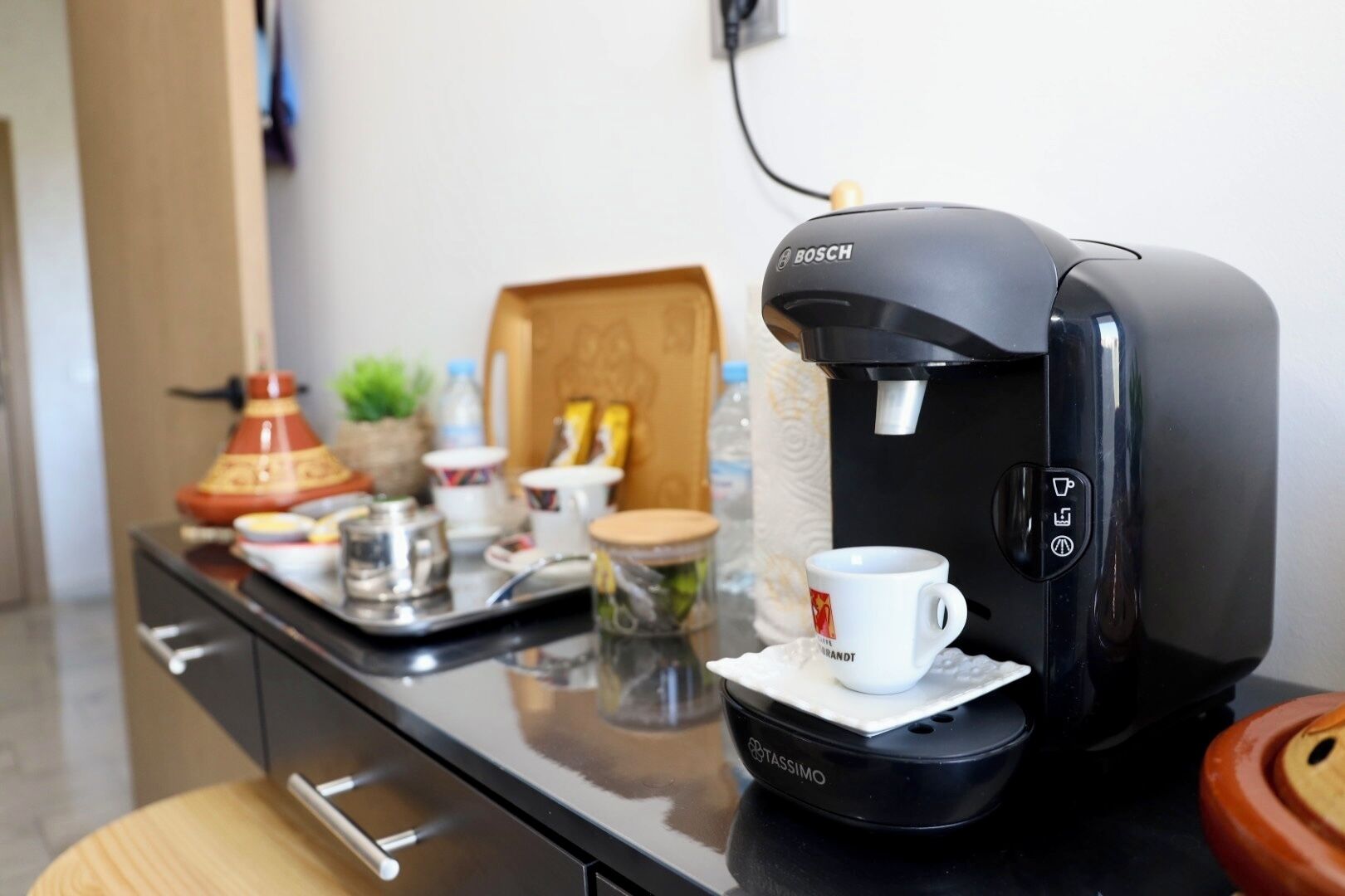 Une machine à café posée sur un plan de travail de cuisine, avec un plateau, une tasse et divers ustensiles de cuisine.