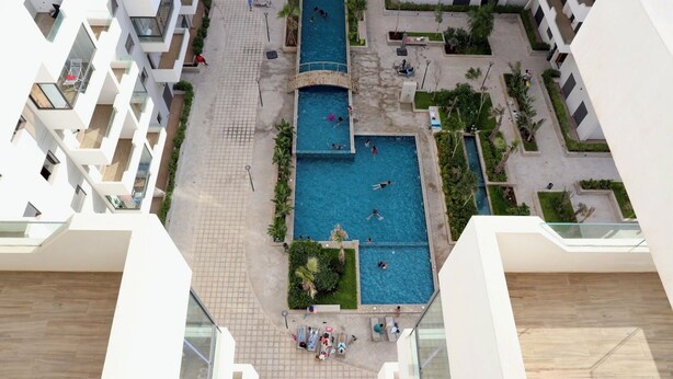 A high-rise building with multiple swimming pools, a central courtyard, and surrounding greenery. - 5mn from the beach, elegant relaxation apartment, Swimming pool, Playground, Park (Âïn-Harrouda)
