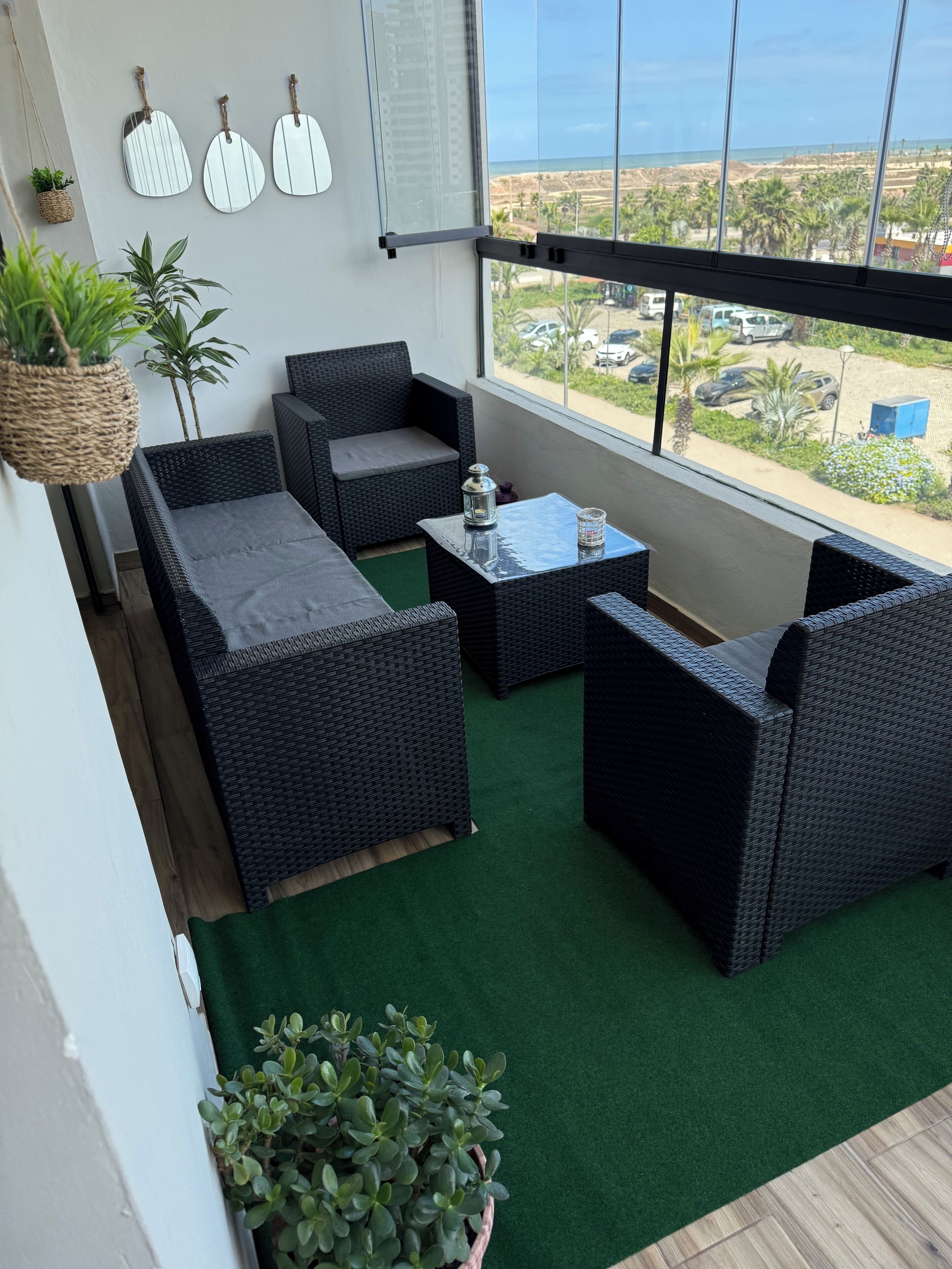 A balcony with wicker furniture, green artificial turf, and potted plants.