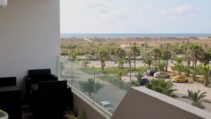 A balcony with a view of a coastal area, including parked cars and palm trees. - 5mn from the beach, elegant relaxation apartment, Swimming pool, Playground, Park (Âïn-Harrouda)