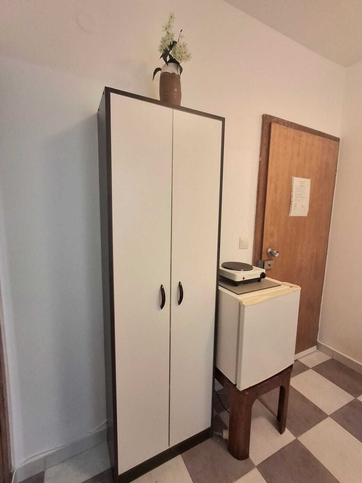 A room with a white wardrobe, a small sink with a mirror, and a wooden door.