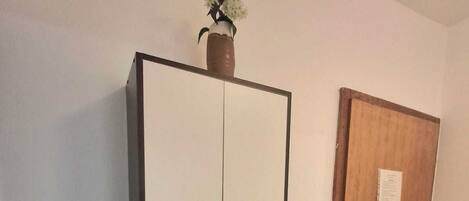 A room with a white wardrobe, a small sink with a mirror, and a wooden door.