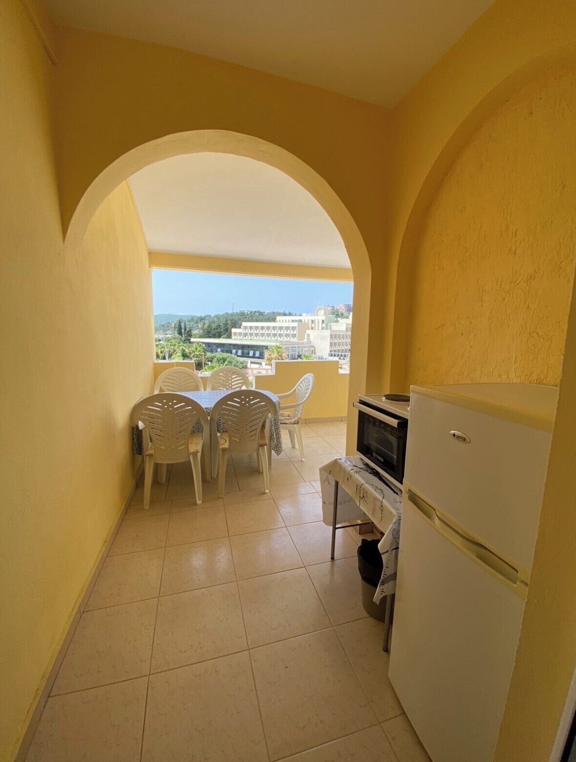 A compact kitchen with a dining area, a refrigerator, and a view of buildings and greenery.