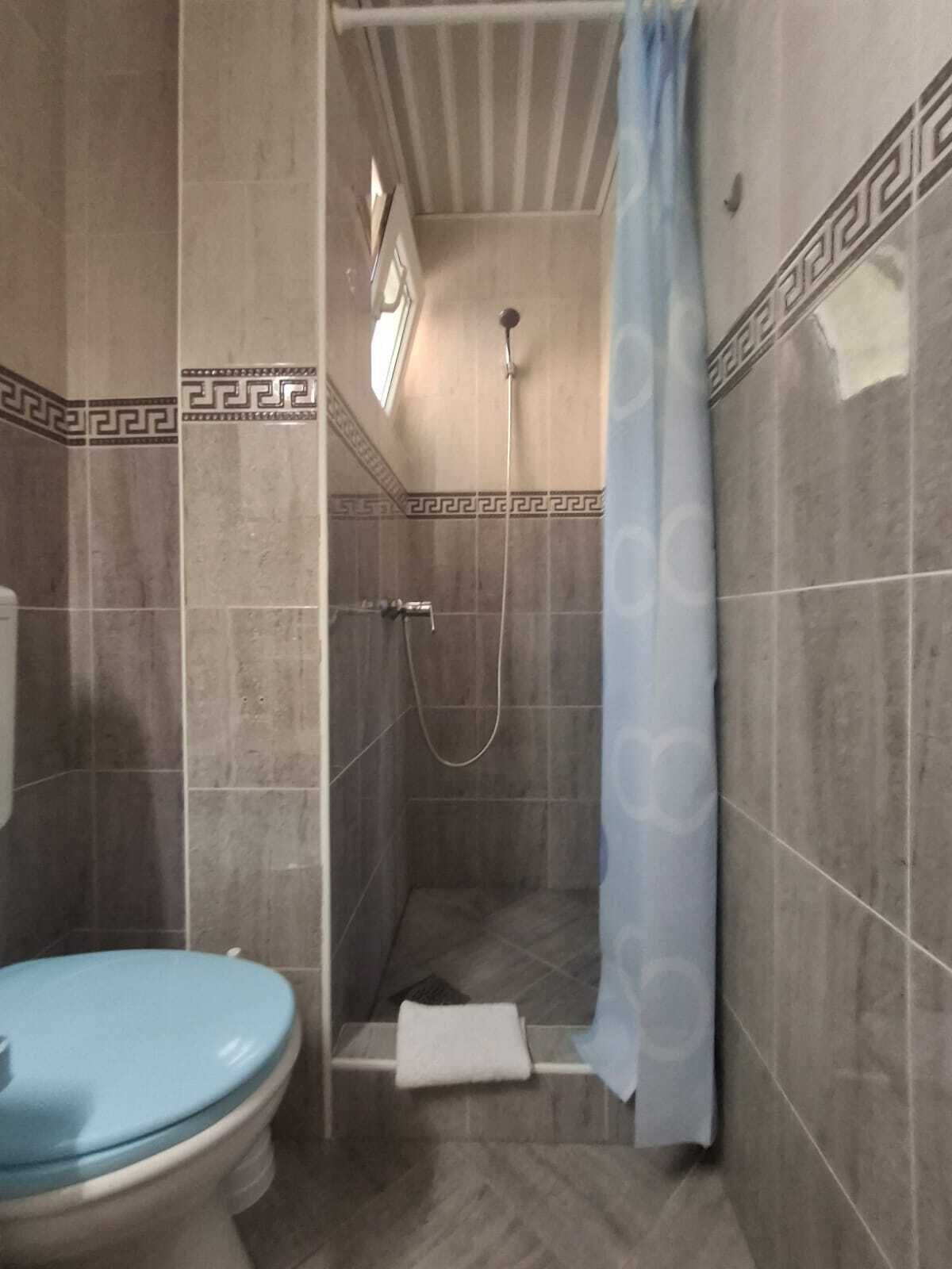 A small bathroom with a toilet, a shower stall with a showerhead, and a towel hanging on the wall.