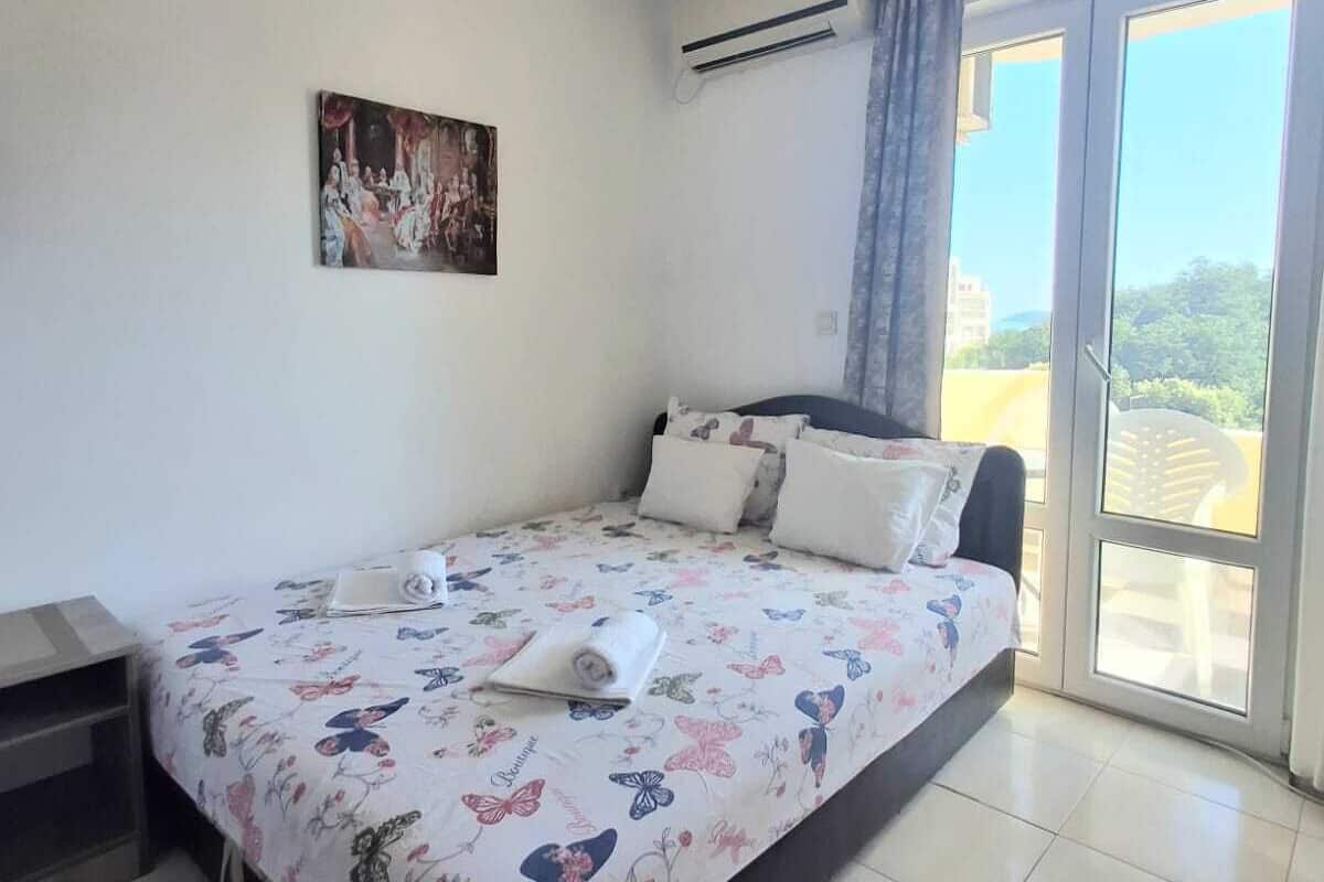 Ein Schlafzimmer mit Bett, einem Bild an der Wand und Blick durch das Fenster.