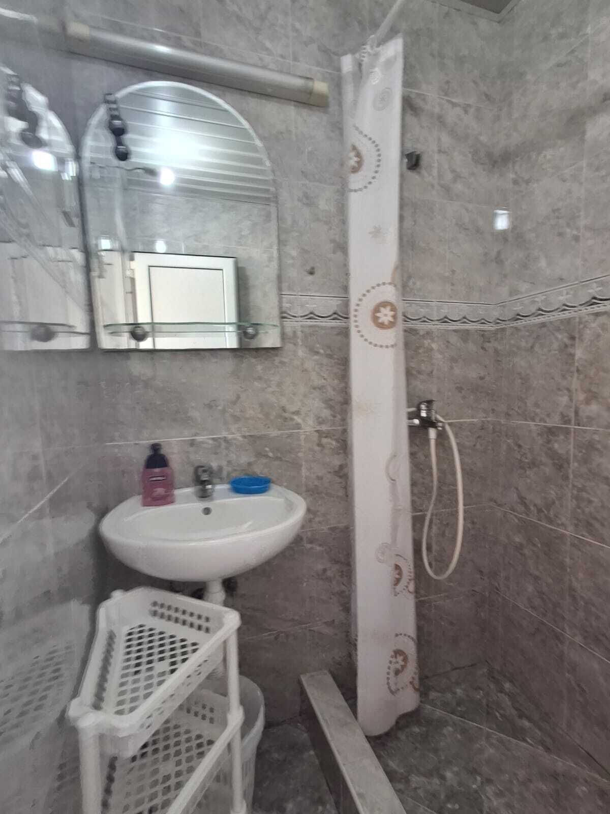 A bathroom with a white sink, a mirror above it, a shower curtain with a floral pattern, and a small white basket.