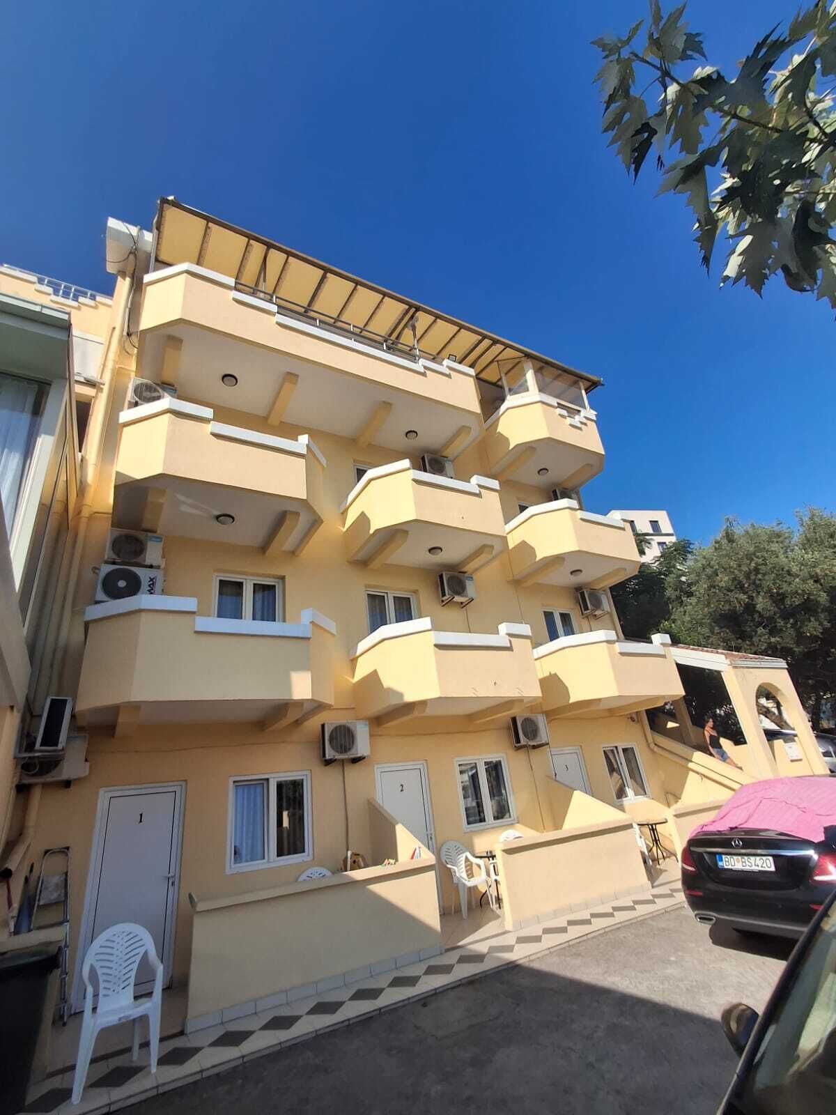 Un edificio de varios pisos con balcones, unidades de aire acondicionado y un coche estacionado en frente.