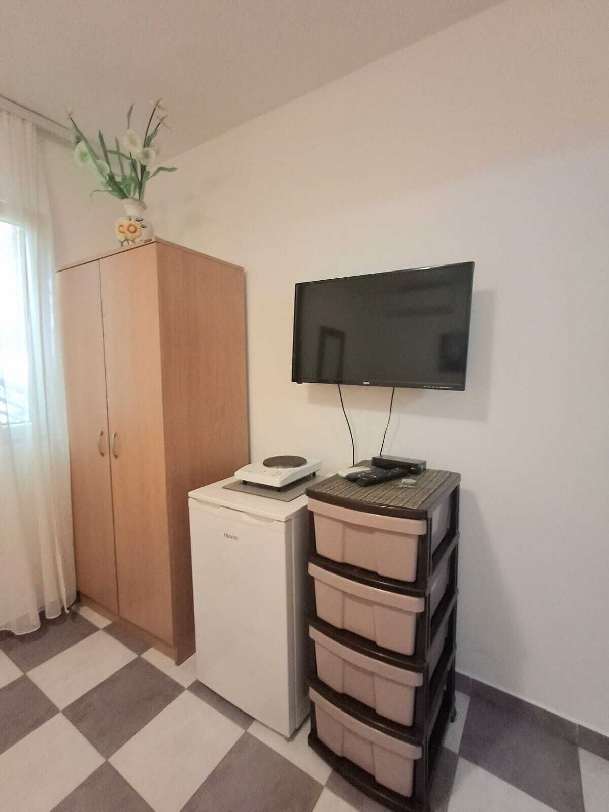 Una habitación con un armario de madera, un mini refrigerador blanco, un televisor sobre un soporte y un juego de cajones.