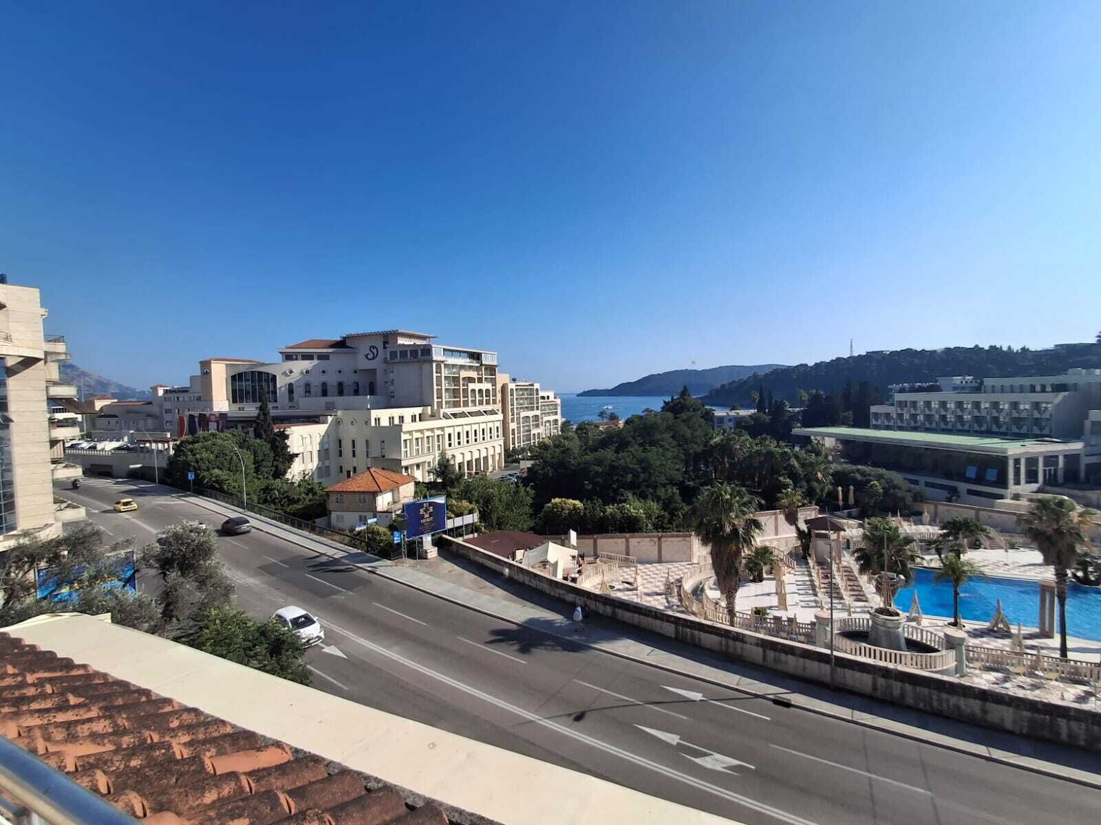 A coastal cityscape with modern buildings, a road, and a swimming pool area.