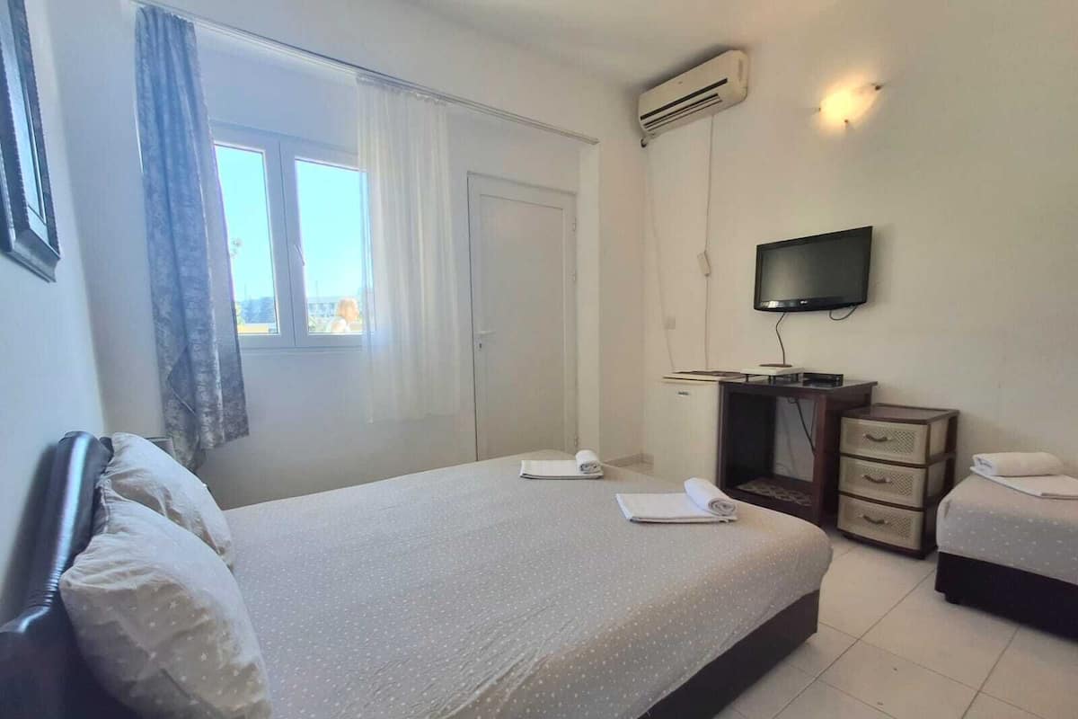 Ein Hotelzimmer mit Bett, Schreibtisch, Fernseher und einem Fenster mit Vorhängen.