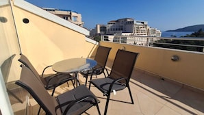 Un balcon avec une table et des chaises, donnant sur un paysage urbain avec des immeubles et une vue sur la mer.