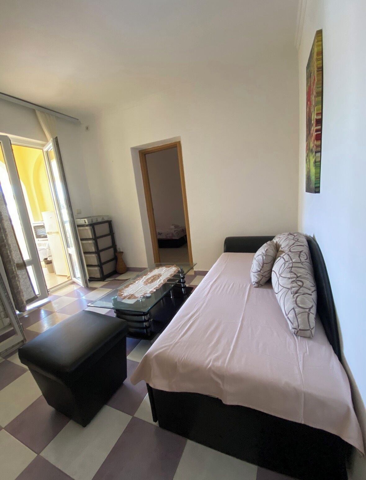 A bedroom with a bed, a bench, a glass table, and a door leading to another room.