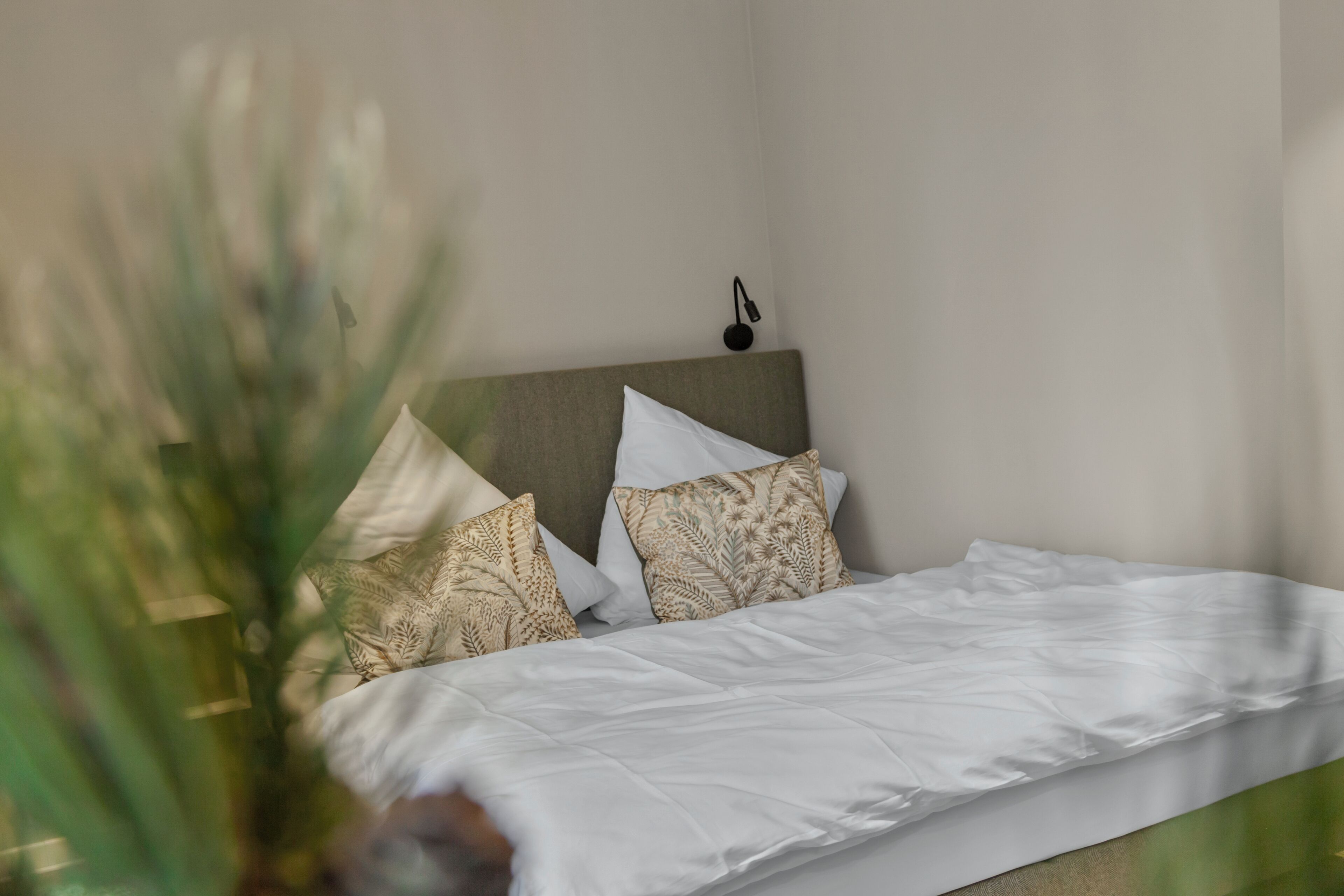 A neatly made bed with white bedding and patterned pillows, a headboard, and a small wall-mounted light fixture.