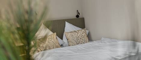 A neatly made bed with white bedding and patterned pillows, a headboard, and a small wall-mounted light fixture.