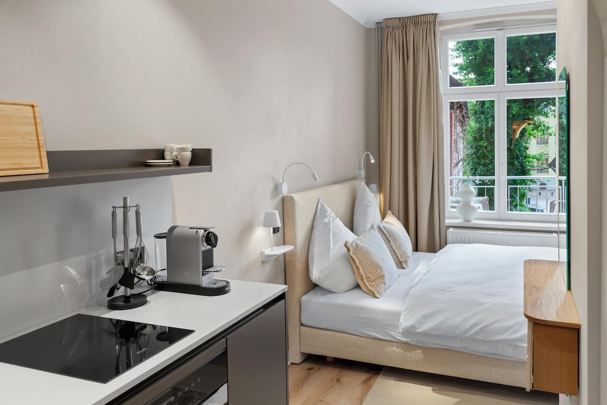 A modern hotel room with a bed, bedside table, and a window with a view of greenery.
