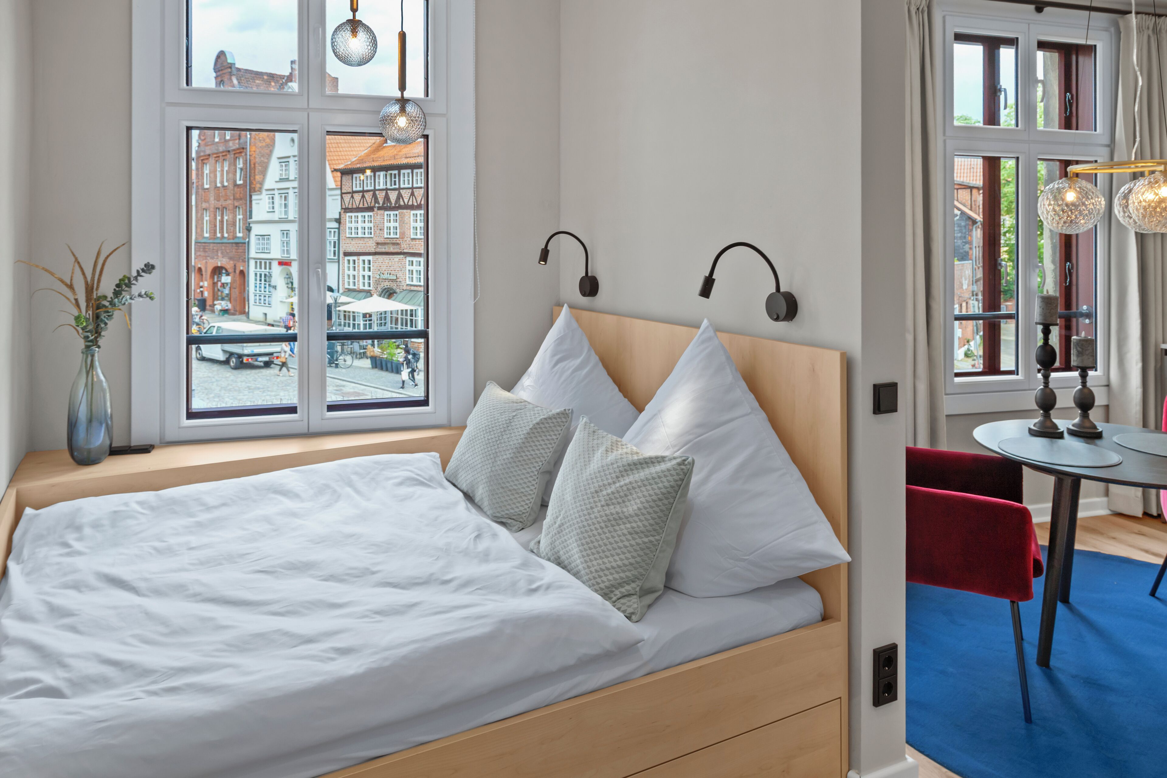 Ein modernes Hotelzimmer mit einem großen Bett, Blick auf die Stadt und einer kleinen Essecke.